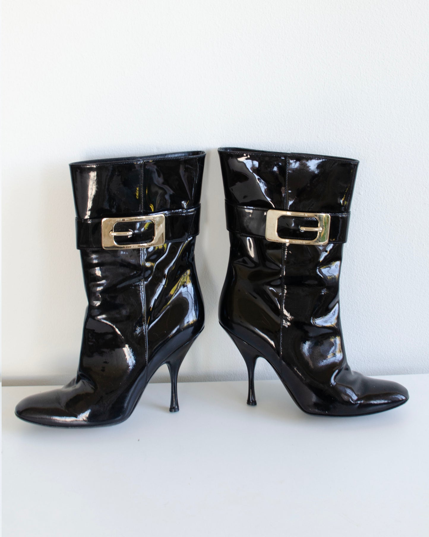 Black Gucci patent leather stiletto ankle booties with metal buckles on a white background