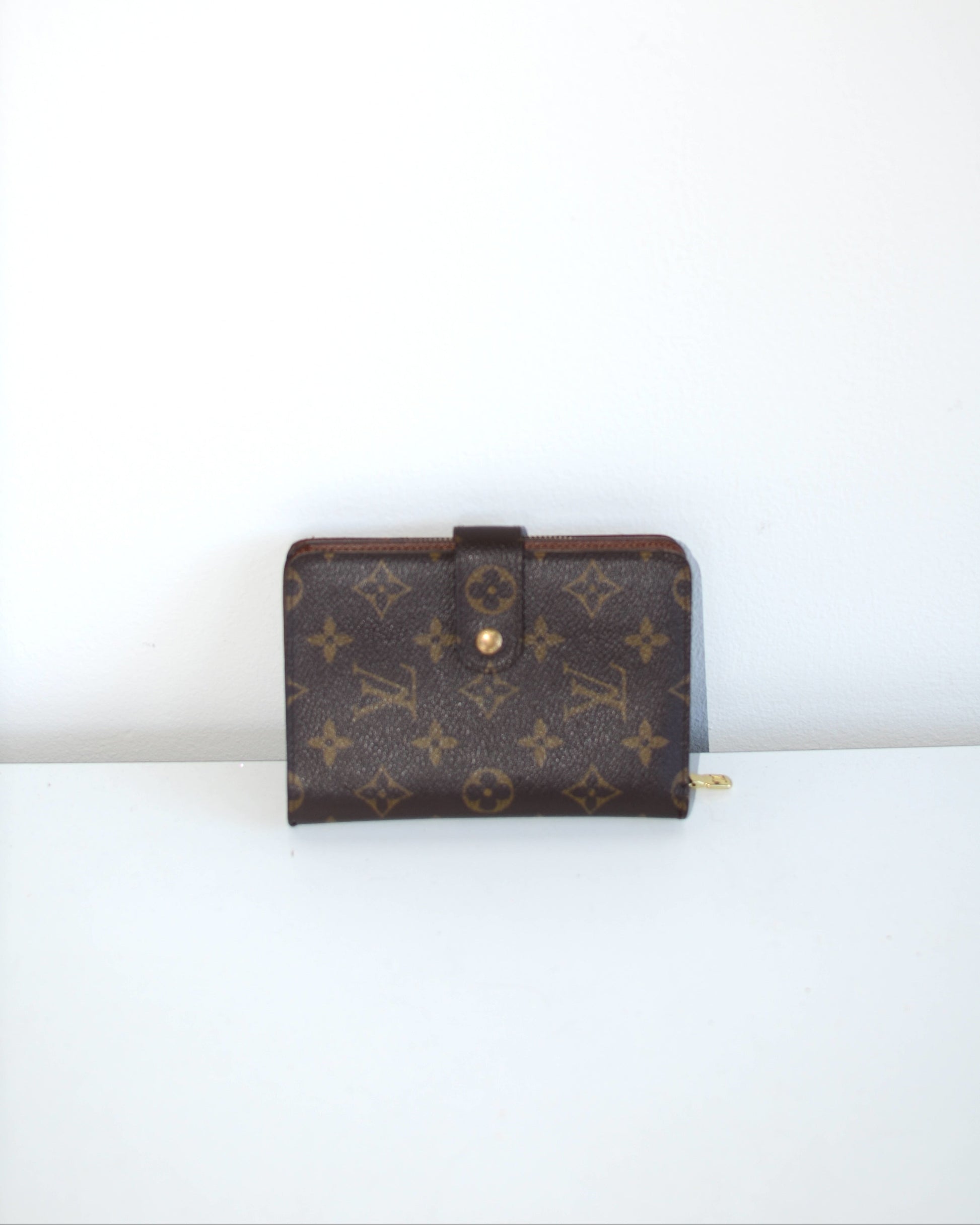 Louis Vuitton compact wallet with buckle and monogram pattern on a white background