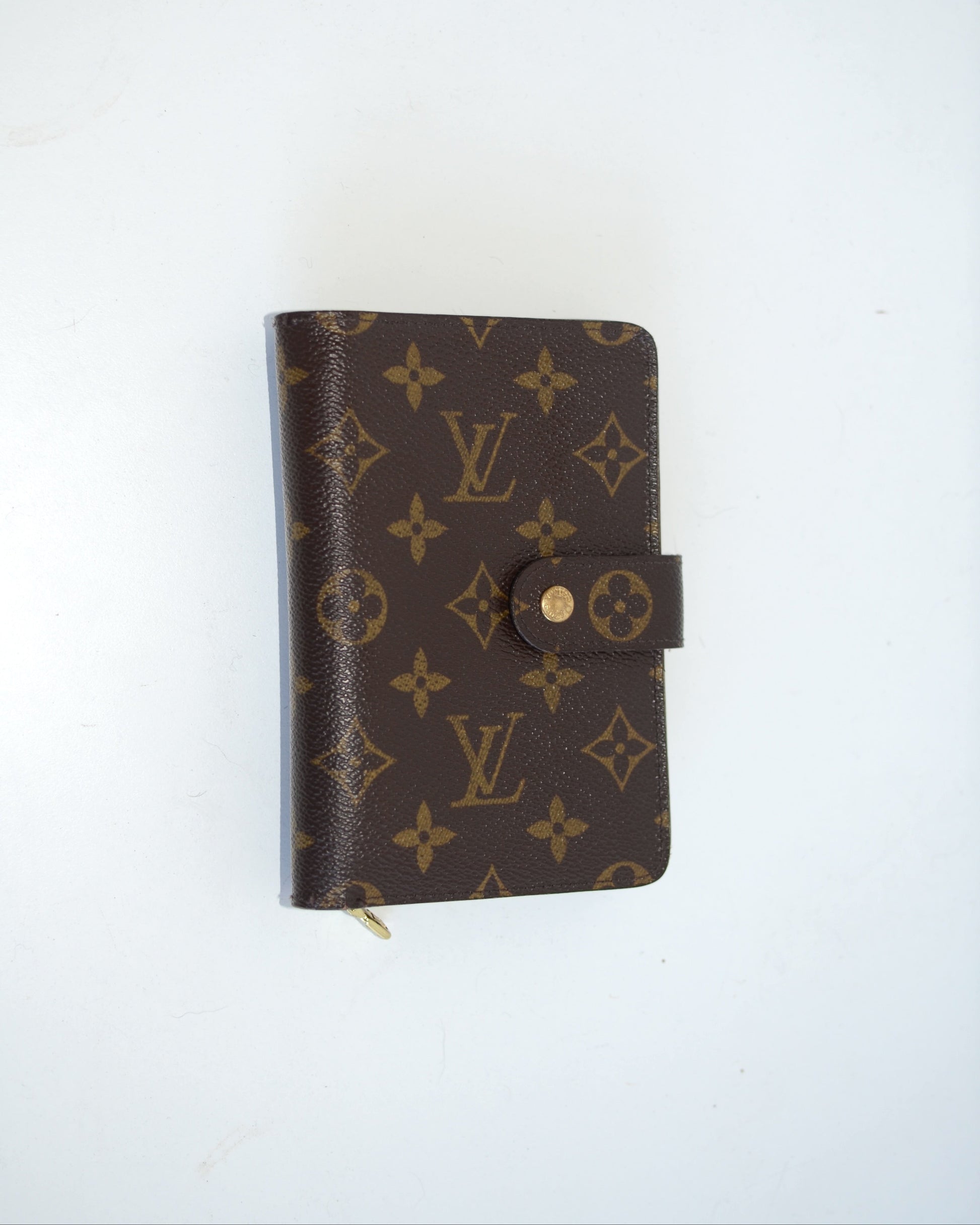 Louis Vuitton compact leather wallet with buckle and monogram pattern on a white background