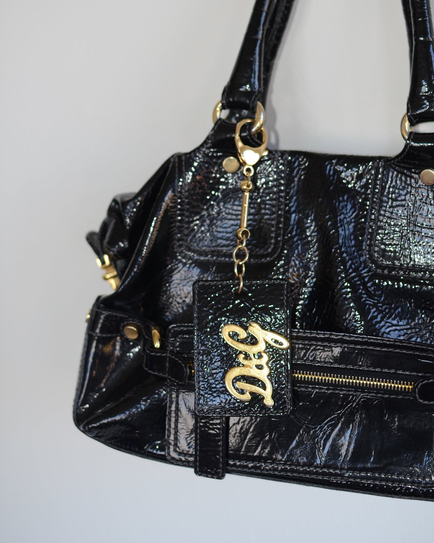 Close up of Dolce & Gabbana Black patent leather handbag with gold accents and hardware, with gold D&G logo charm on a white background