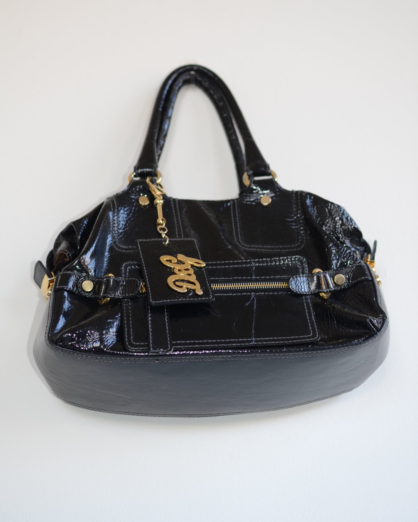 Bottom view of Dolce & Gabban Black patent leather handbag with gold accents and hardware, with gold D&G logo charm on a white background