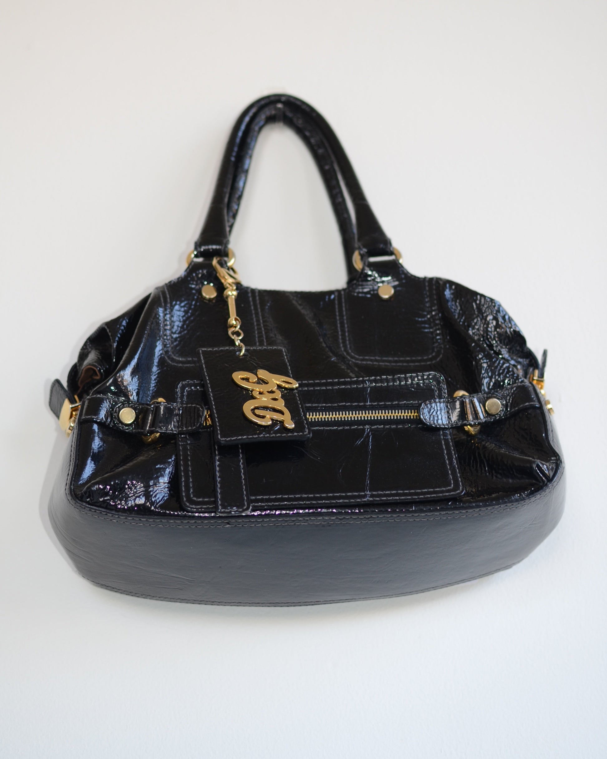 Bottom view of Dolce & Gabban Black patent leather handbag with gold accents and hardware, with gold D&G logo charm on a white background