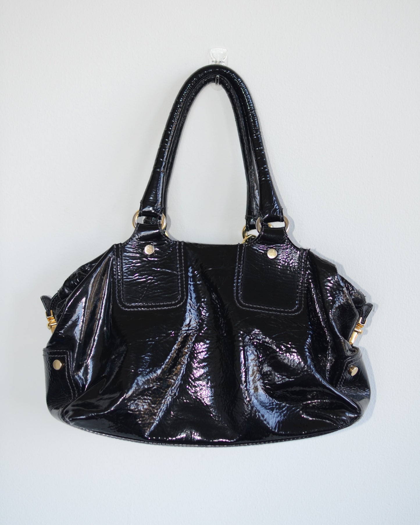 Back view of Dolce & Gabbana Black patent leather handbag with gold accents and hardware, with gold D&G logo charm on a white background