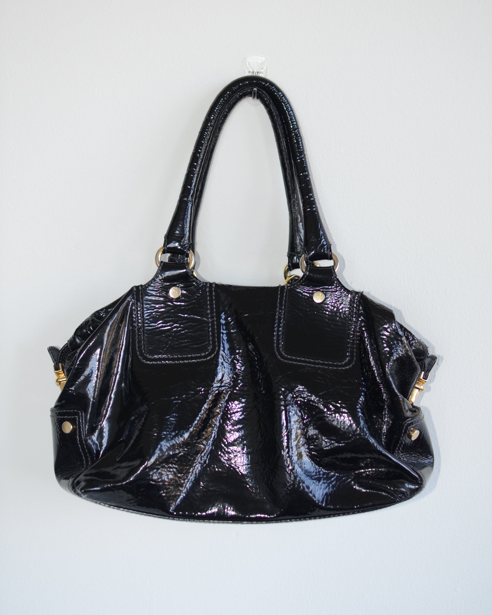 Back view of Dolce & Gabbana Black patent leather handbag with gold accents and hardware, with gold D&G logo charm on a white background