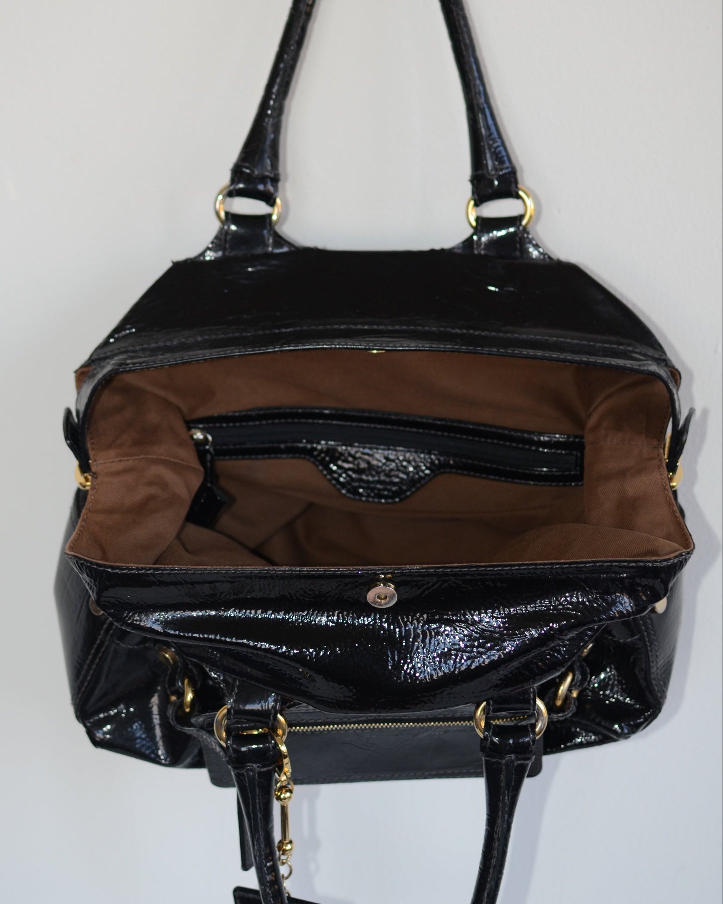 Inside lining of Dolce & Gabbana Black patent leather handbag with gold accents and hardware, with gold D&G logo charm on a white background