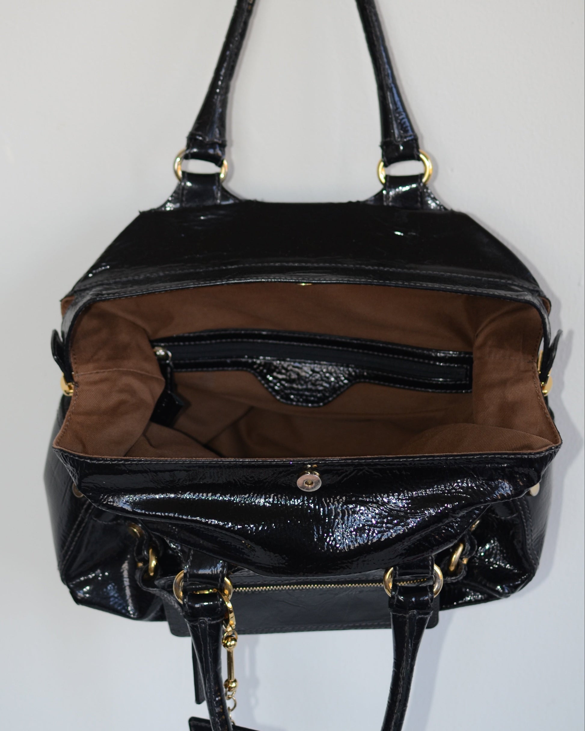 Inside lining of Dolce & Gabbana Black patent leather handbag with gold accents and hardware, with gold D&G logo charm on a white background