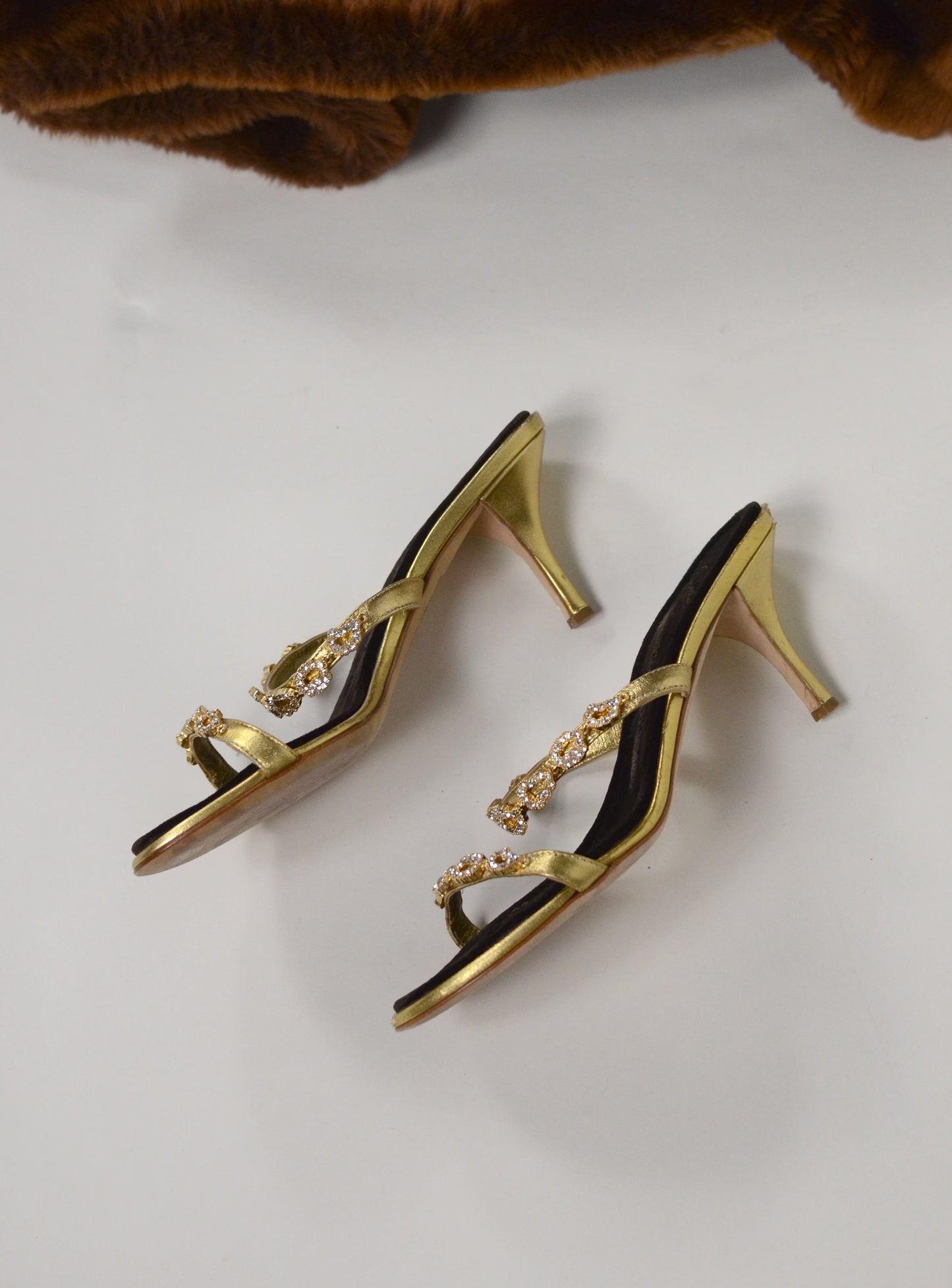 Gold high-heeled  Giuseppe Zanotti sandals, close up on gold straps with  embellishments and brown velvet sole on a white surface.