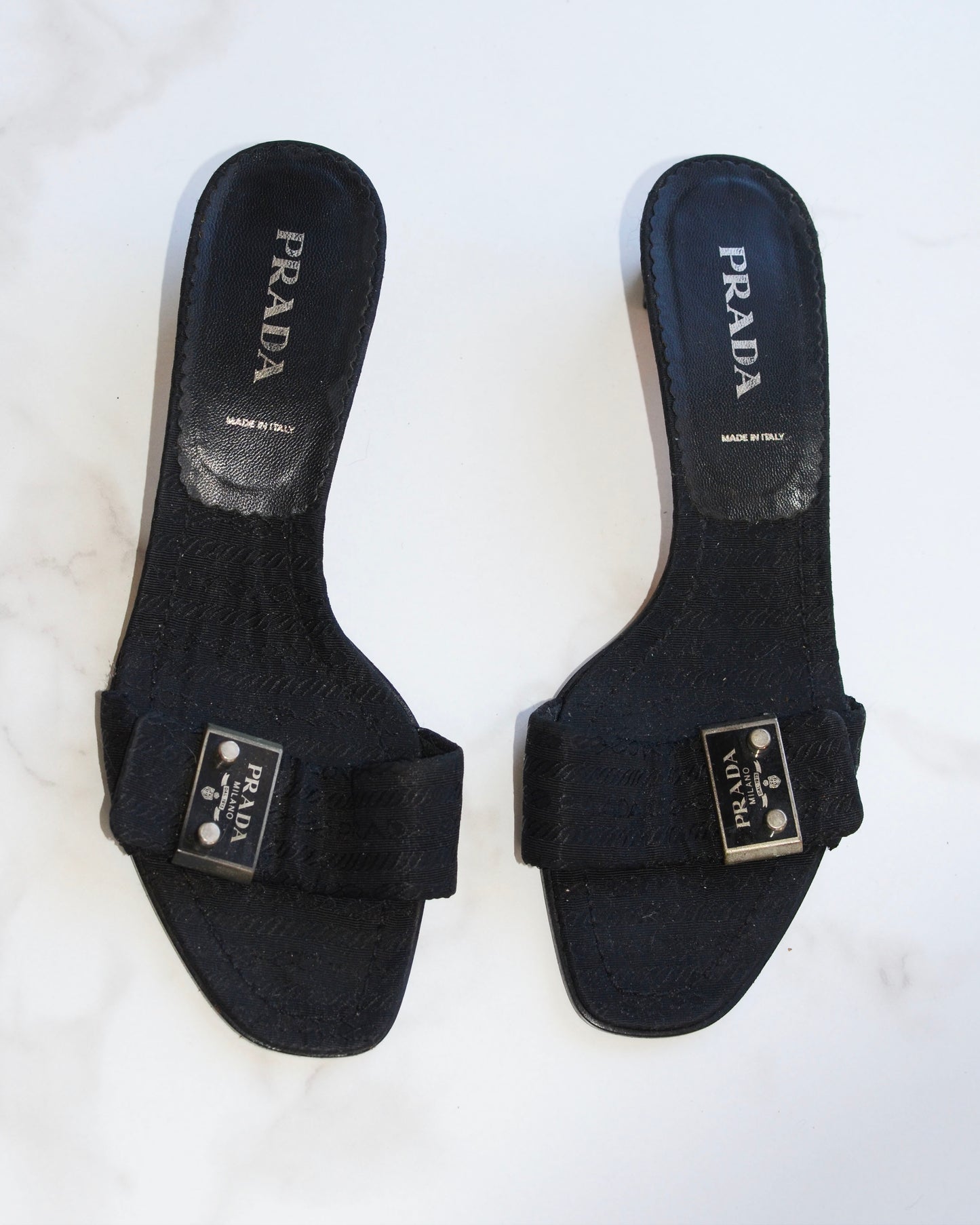 Pair of vintage black Prada sandals with metal logo on a white background
