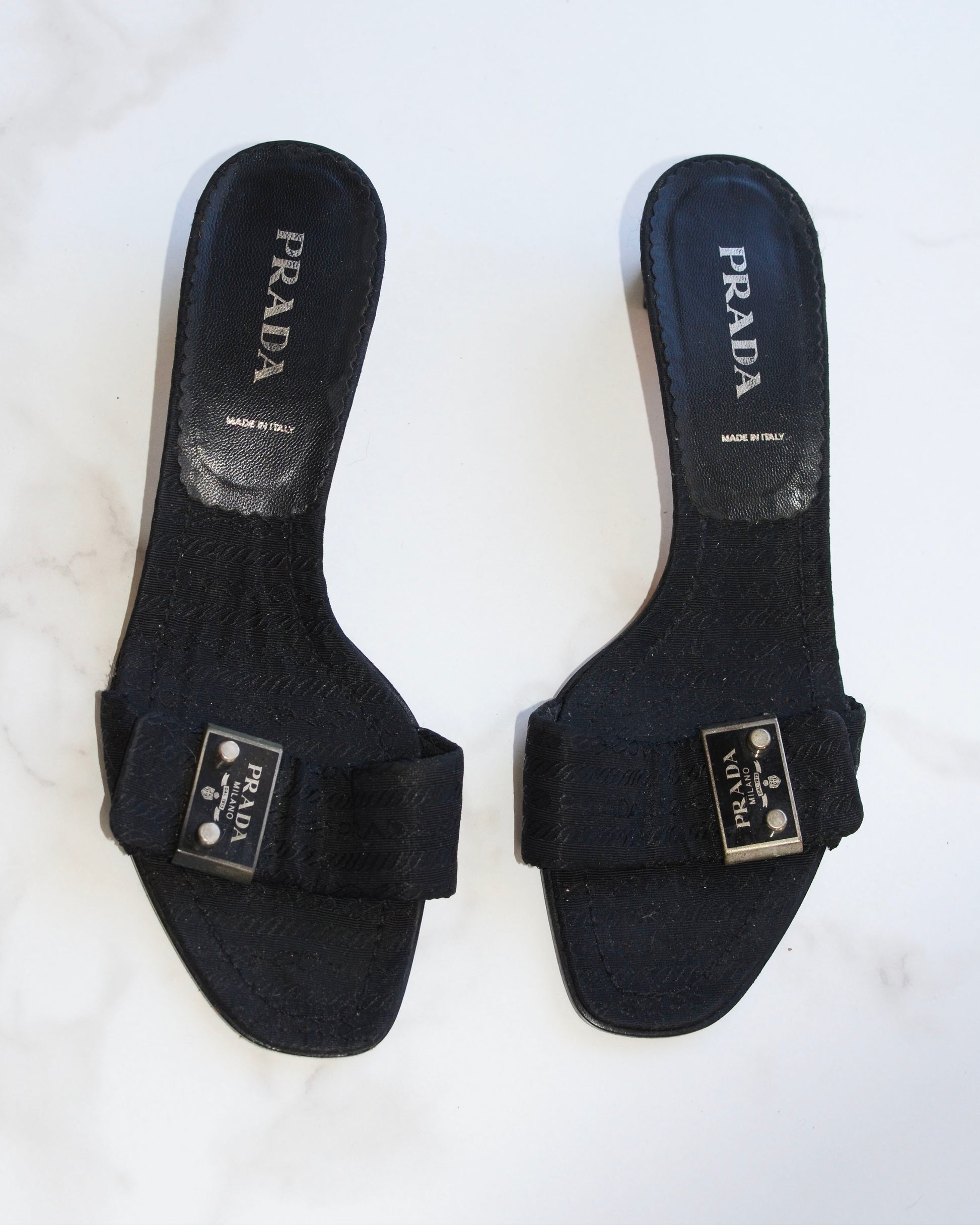 Pair of vintage black Prada sandals with metal logo on a white background