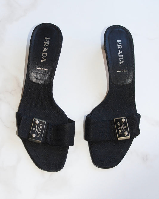 Pair of vintage black Prada sandals with metal logo on a white background