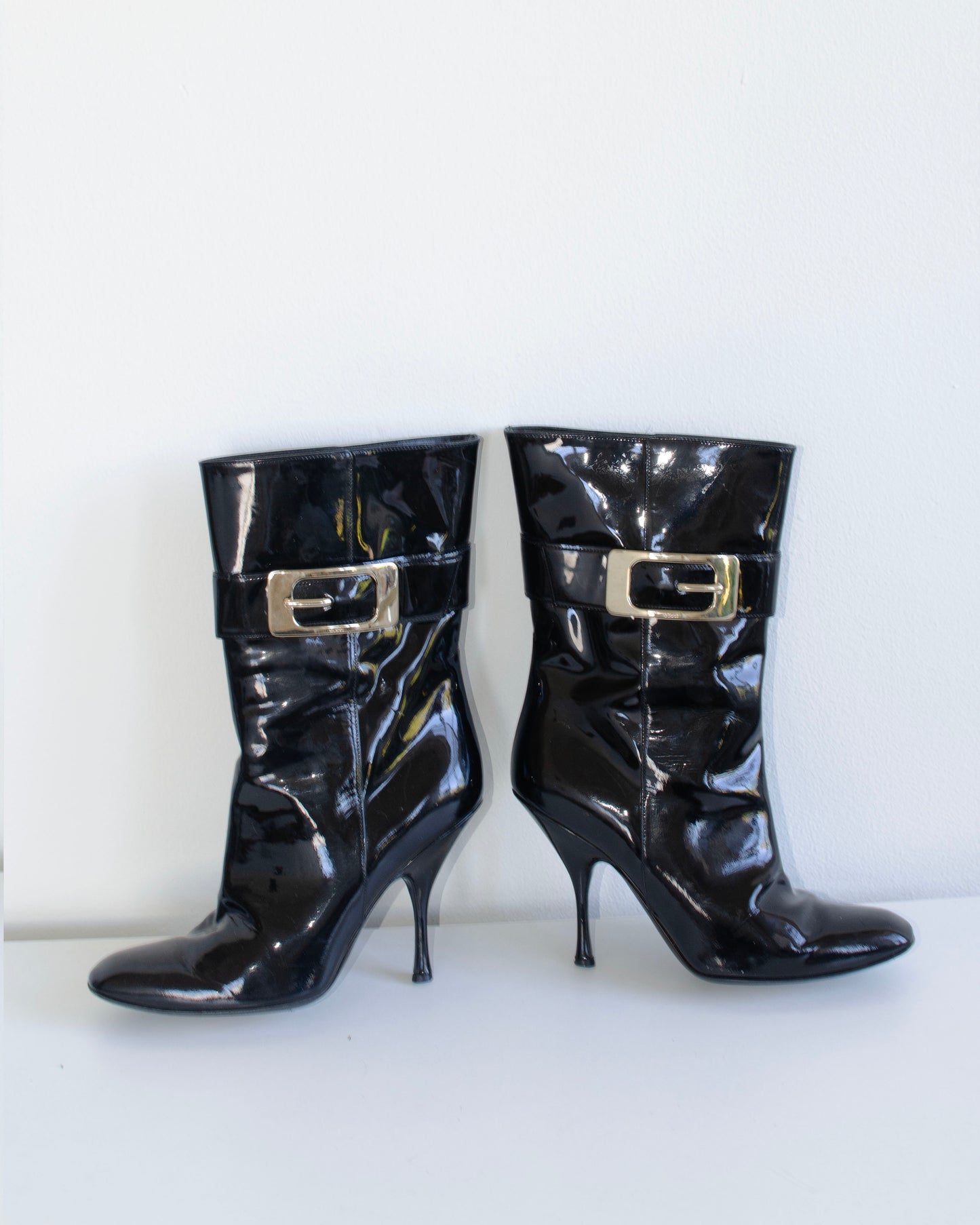 Black  Gucci patent leather stiletto ankle booties with metal buckles on a white background