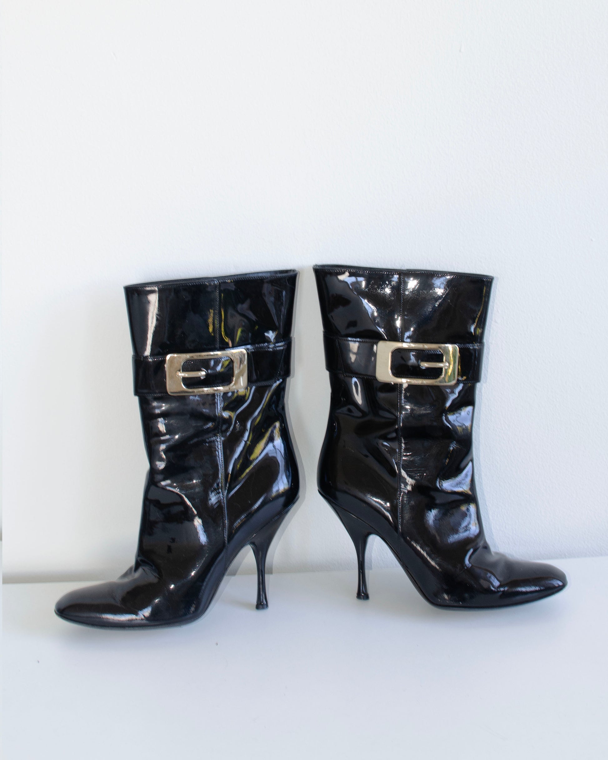 Black  Gucci patent leather stiletto ankle booties with metal buckles on a white background