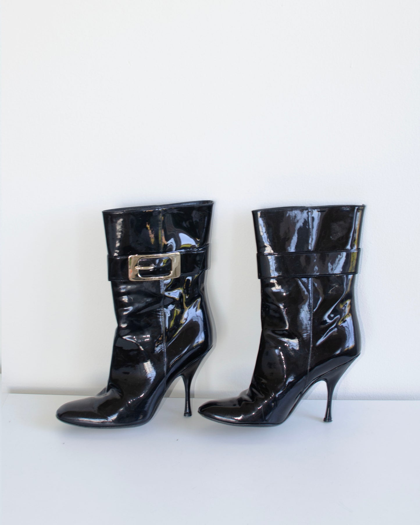 Black  Gucci patent leather stiletto ankle booties with metal buckles on a white background