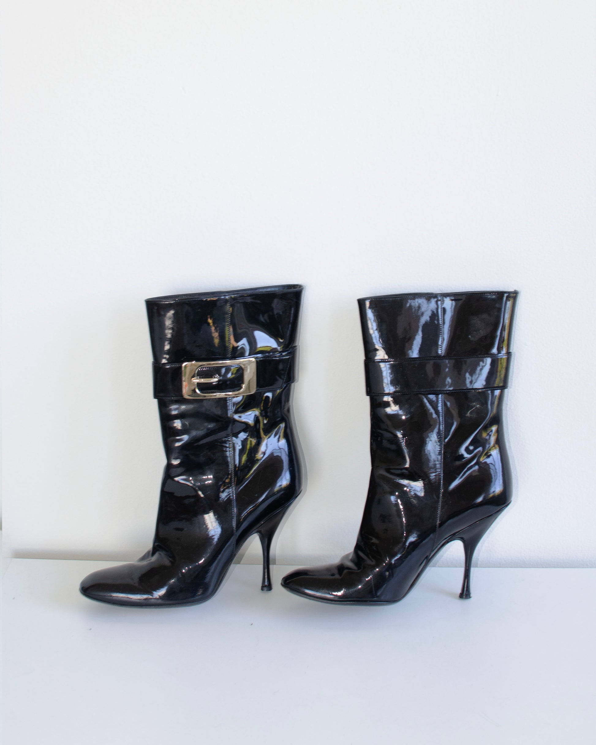 Black  Gucci patent leather stiletto ankle booties with metal buckles on a white background