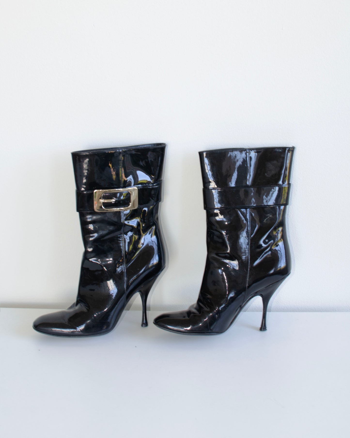 Black  Gucci patent leather stiletto ankle booties with metal buckles on a white background