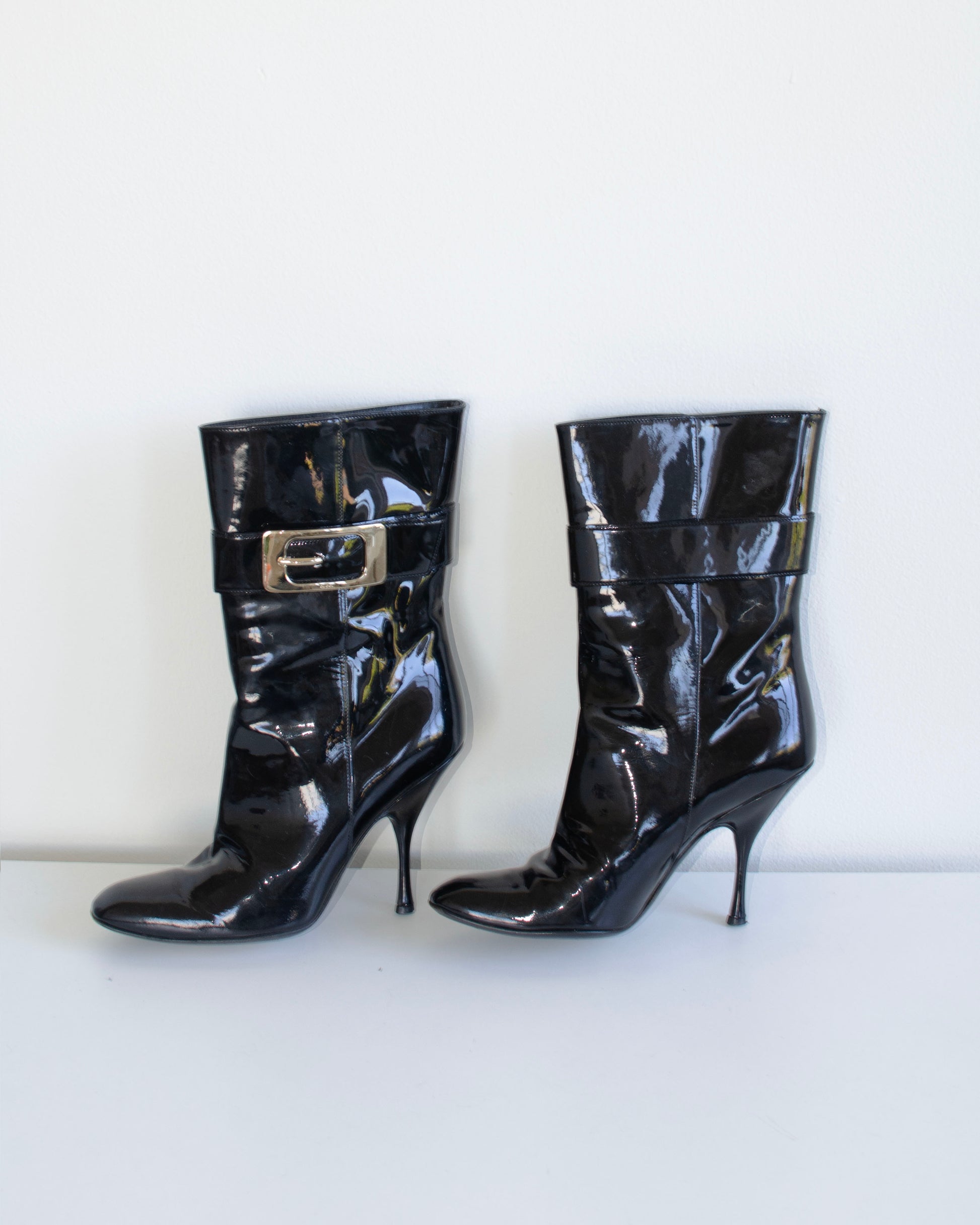 Black  Gucci patent leather stiletto ankle booties with metal buckles on a white background